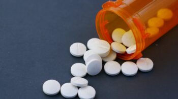 Close-up of white pills scattered from an orange prescription bottle on a gray surface.