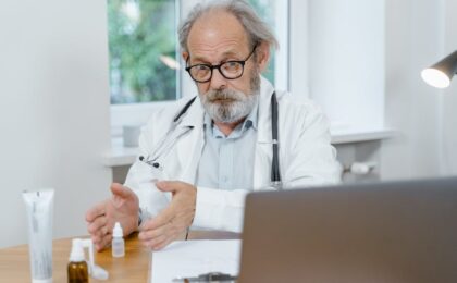 An elderly doctor in a white coat conducting an online medical consultation, focusing attentively.
