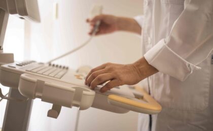 Healthcare worker operating advanced ultrasound machine in medical setting.