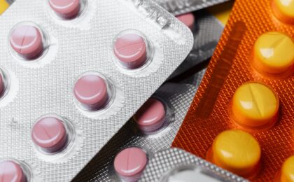 From above closeup mix of various multicolored round pills of different sizes in plastic blister packs under bright ligh