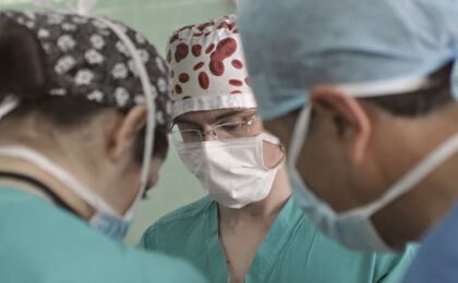 Team of doctors in surgical attire performing a medical procedure in an operating room.
