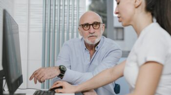 Elderly man receiving consultation from a medical practitioner in a modern indoor setting.